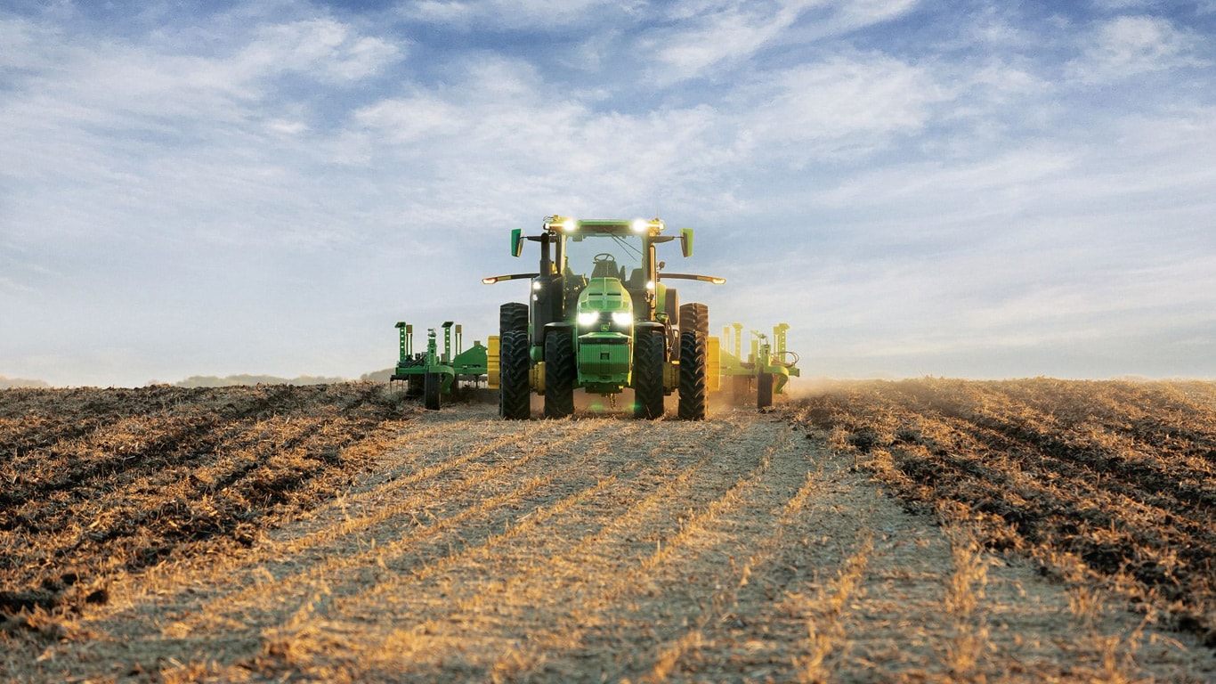 Самоходен трактор John Deere, който тегли оборудването за обработка на почвата през открито поле.