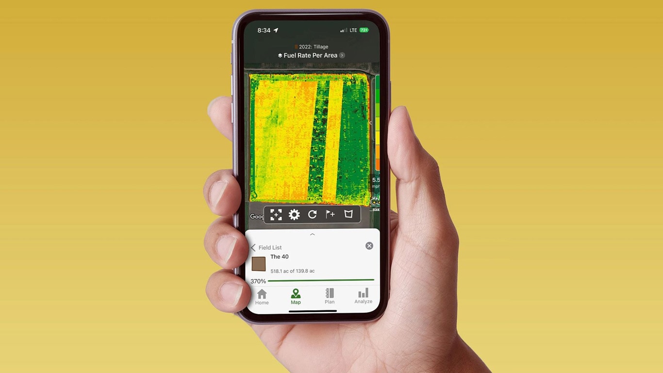 Ръка, държаща смартфон, показващ John Deere Operations Center с данни за разхода на гориво.