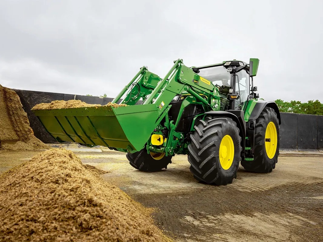 Кофата на челния товарач е пълна със силаж на трактор John Deere по време на работа по обработка на материала.