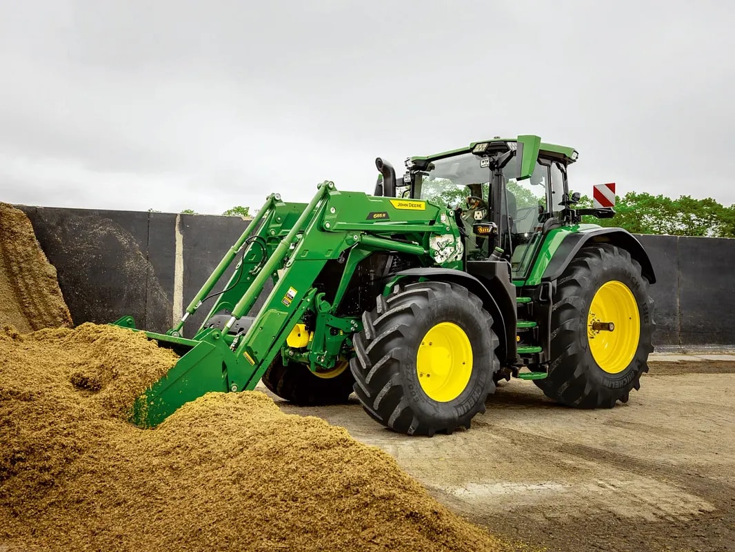 Трактор John Deere с челен товарач избутва силаж в силажна яма във фермерска среда.