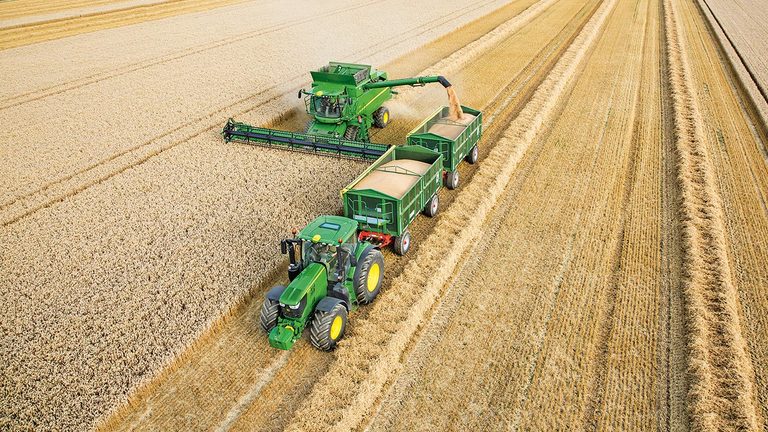 Комбайн от серия S на John Deere, разтоварващ пшеница в двойни ремаркета, теглени от трактор