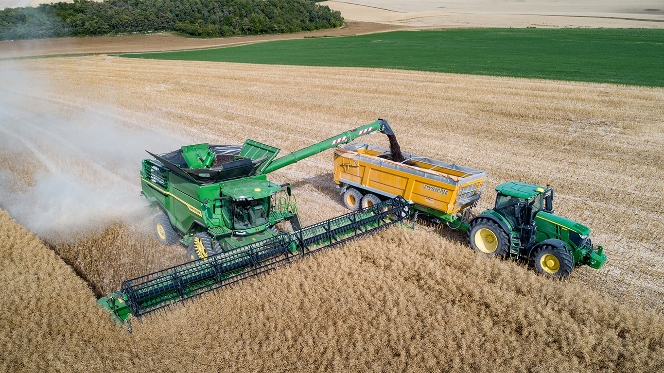 Комбайн от серия Х на John Deere, разтоварващ рапично семе в ремарке за зърно, теглени от трактор на John Deere