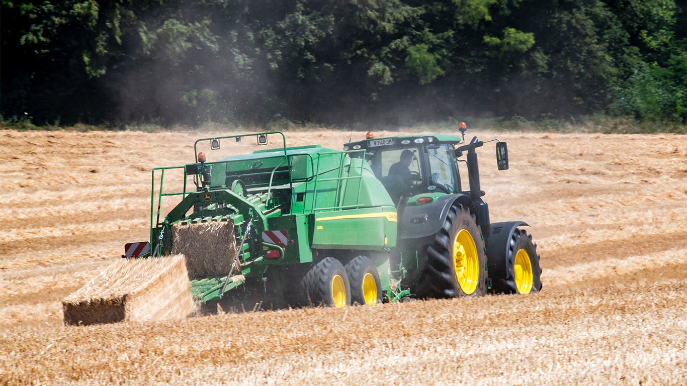 Голяма квадратна балопреса John Deere L634 с трактор 6R в слама