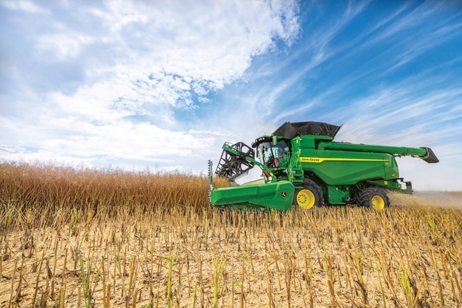 Комбайн John Deere жъне зърно с хедер на полето под синьо небе по време на жътва на култура