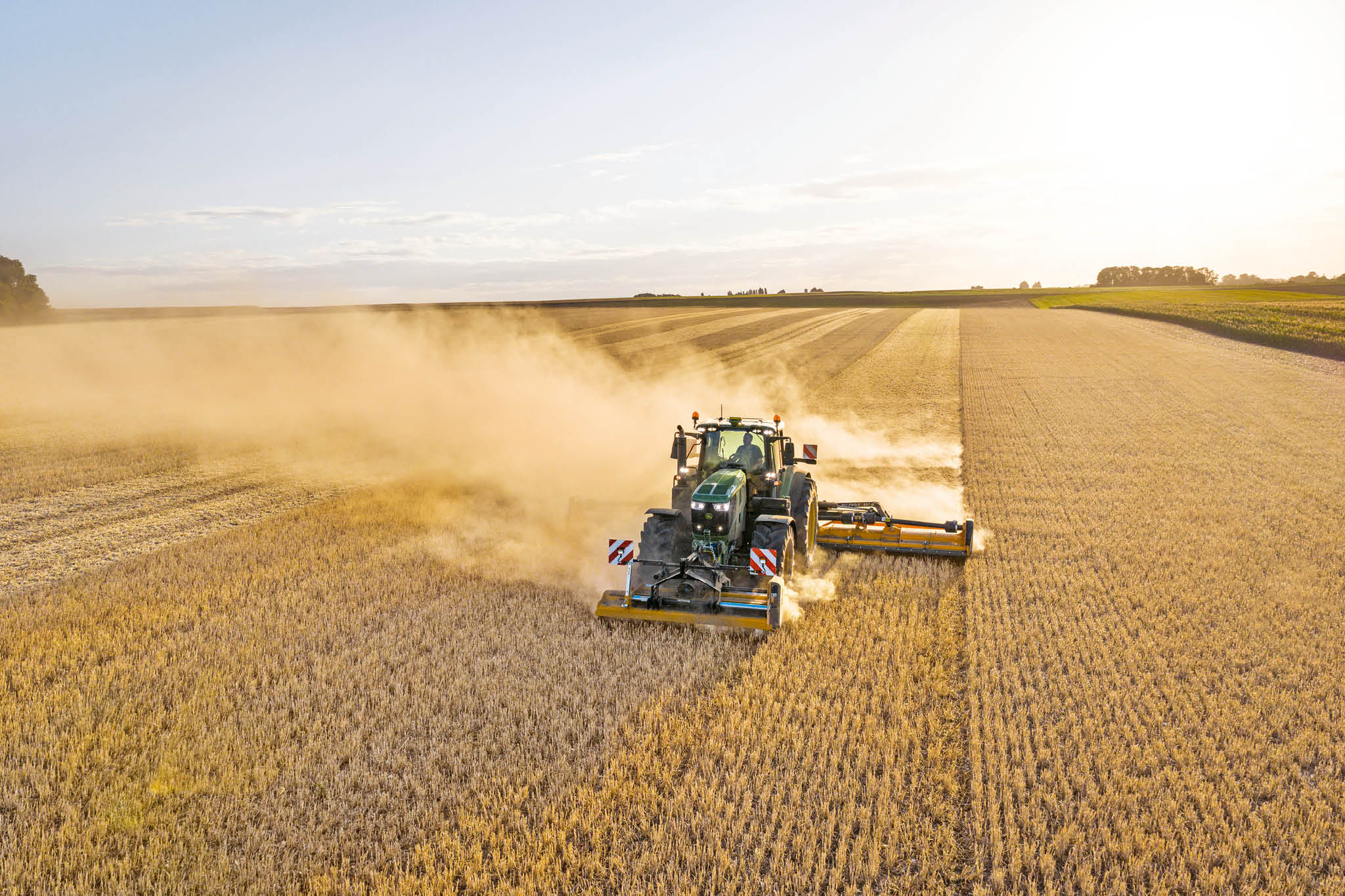 Трактор John Deere от серия 6M, който тегли цистерна за течен тор по селски път, ограден от трева и полета.
