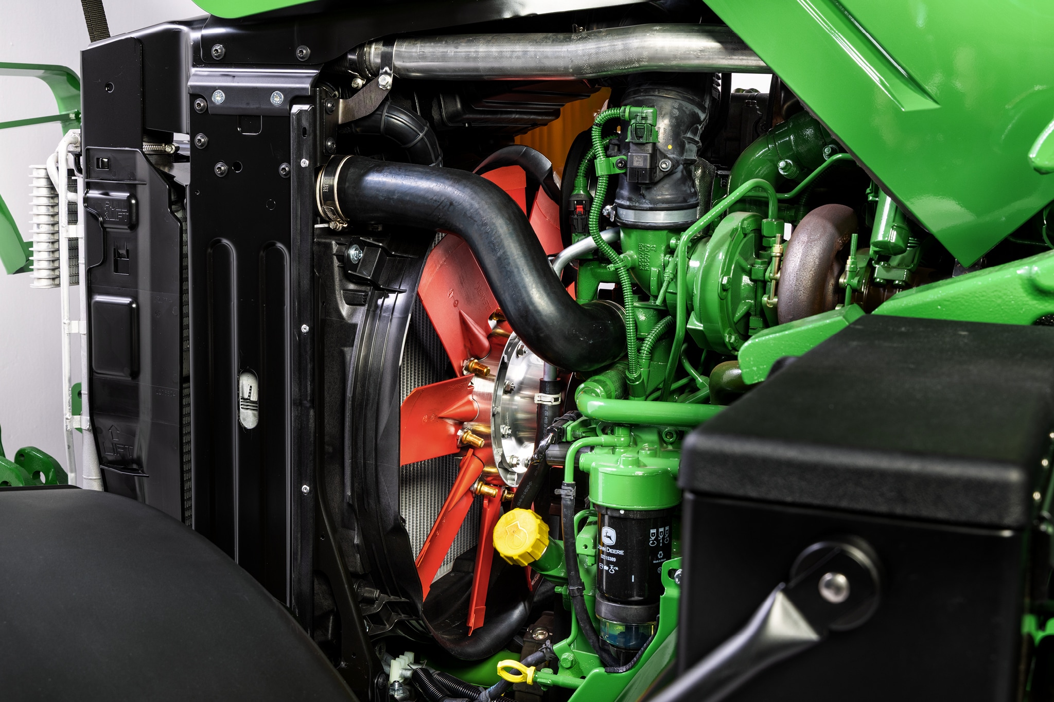 Изглед отблизо на двигателното отделение от серия 6M на John Deere, което акцентира върху охладителната система и компонентите на двигателя.