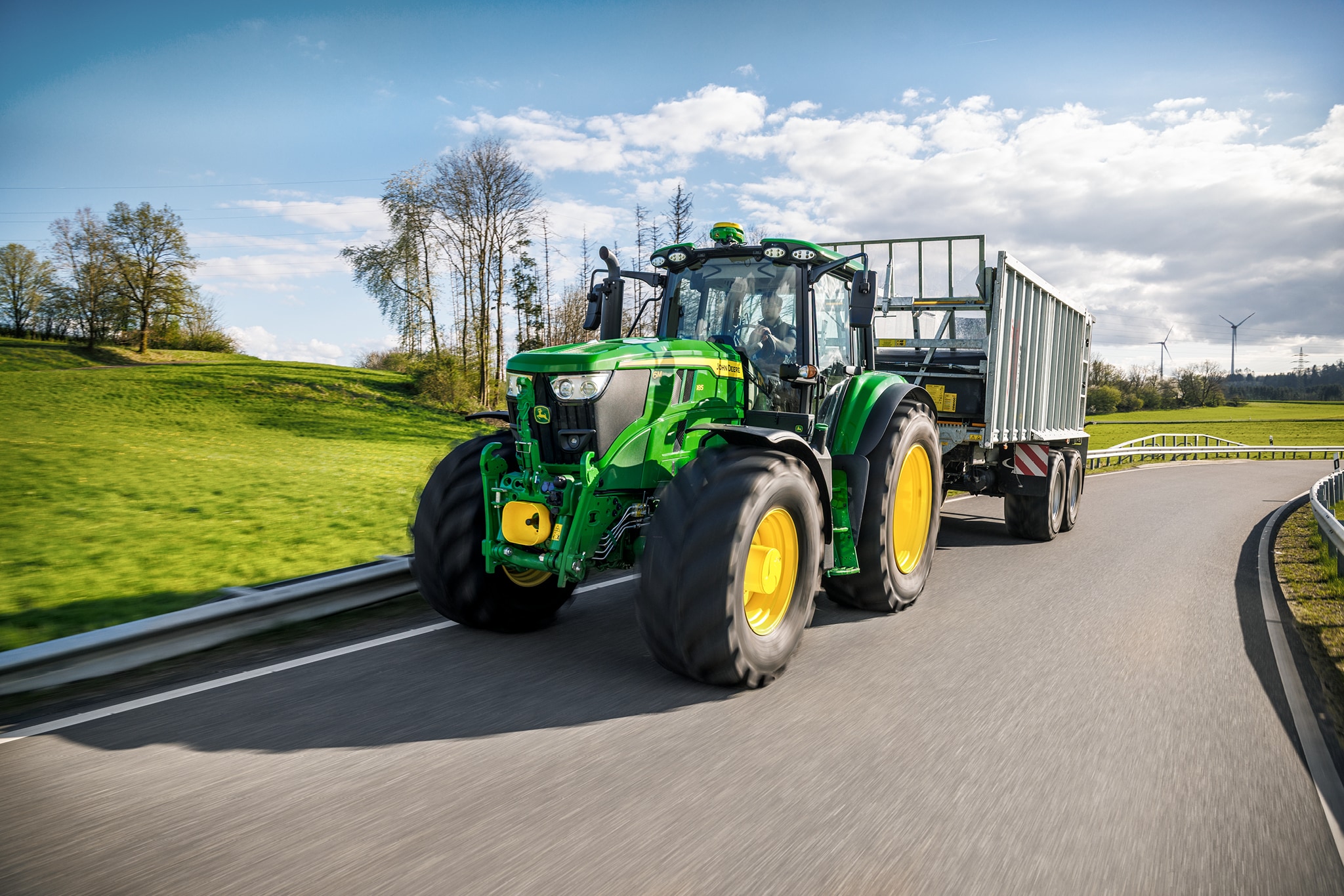 Трактор John Deere от серия 6M, превозващ ремарке от високата страна по настилка в селските райони.
