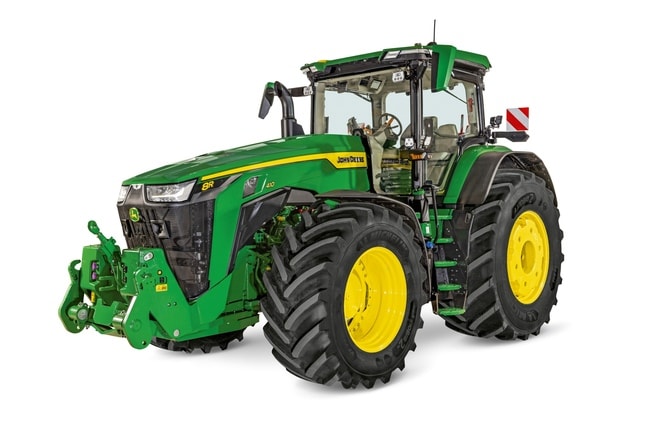 Трактор 8R на John Deere със затворена кабина, големи селскостопански гуми и предна навесна система, показани в бяло студио.
