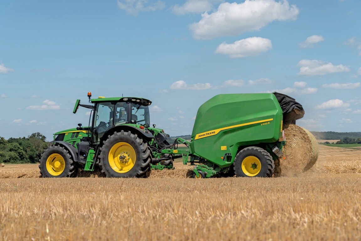 John Deere V452R на поле със слама, теглен от John Deere 6R 150, който изхвърля бала