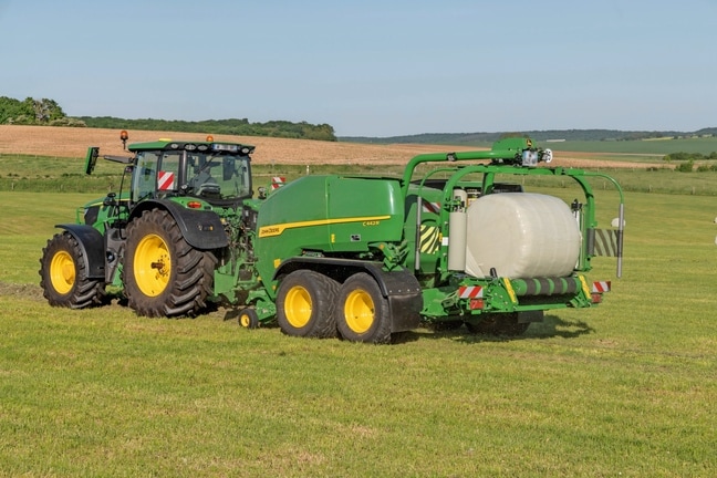 Опаковащ балировач John Deere C442R, теглен от трактор John Deere 6R 185, оформяща бали със силоз с висока плътност
