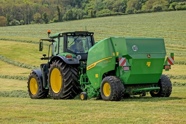 Балопреса John Deere F442M, теглена от трактор John Deere 6M на хълмисто тревисто поле