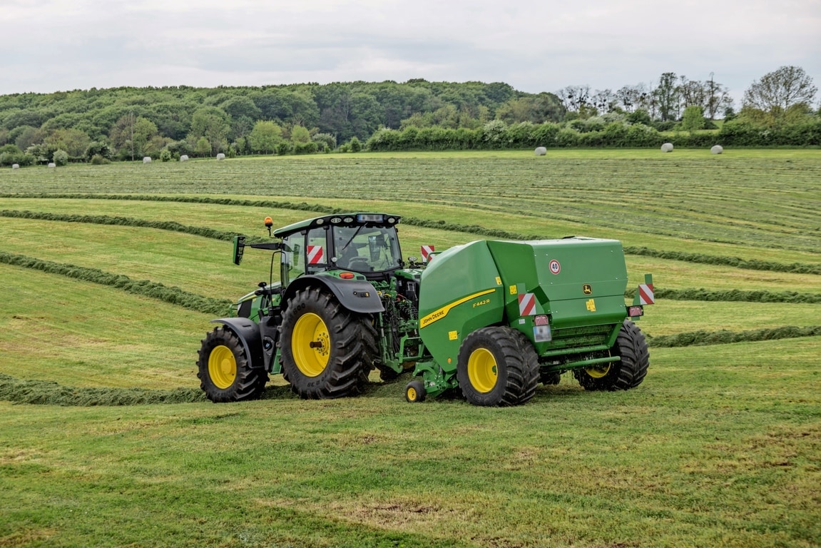 Балопреса John Deere F442R, теглена от трактор John Deere 6M на хълмисто тревисто поле