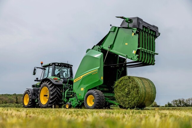 Балопреса John Deere V462M, теглена от трактор John Deere 6M, изхвърляща бала с трева